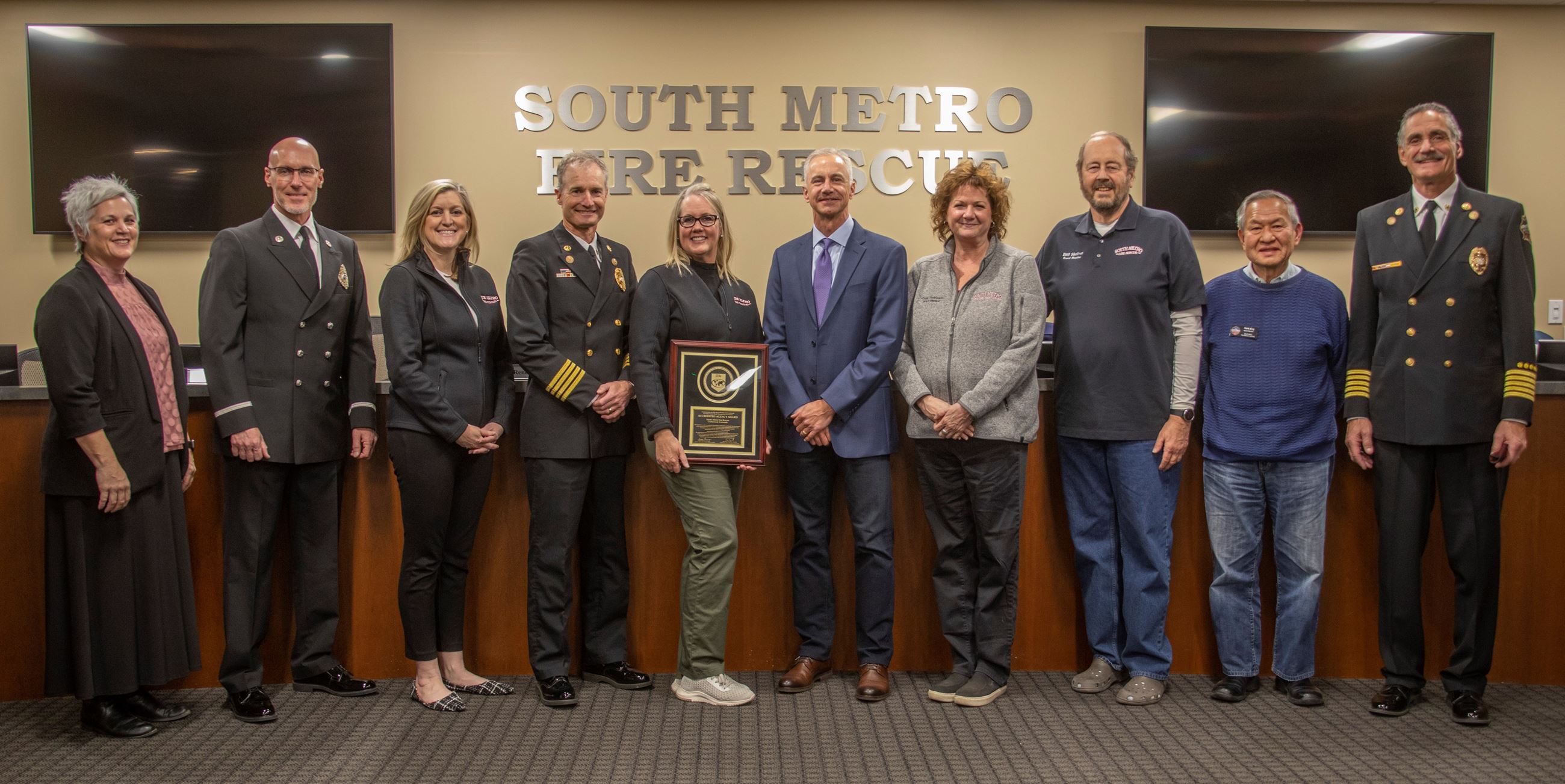 Group of people standing with an accreditation award in front of the South Metro Fire Rescue sign